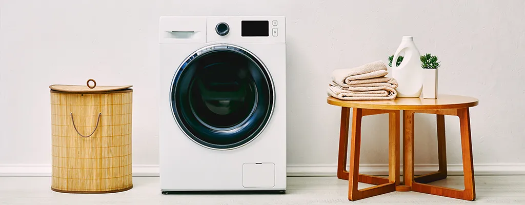 washing machine next to laundry basket and table with laundry on it