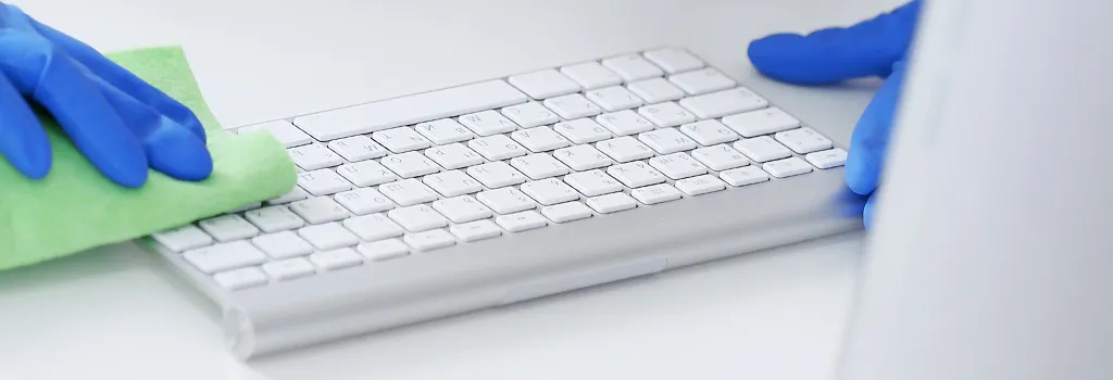 hands in rubber gloves wiping computer keyboard with cloth